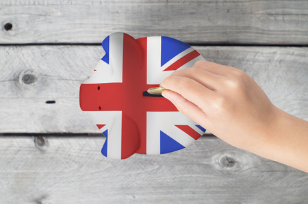 United Kingdom saving concept with little hand dropping a coing into piggy bank overlaid with UK flagの写真素材