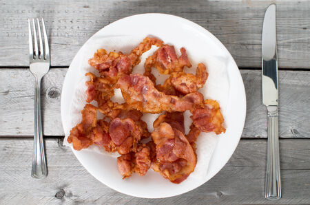 Fried bacon on a ceramic plate against wooden background with knife and forkの写真素材