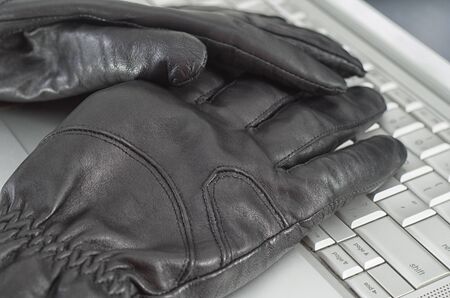 Hacking concept with pair of black leather gloves over metallic laptop keyboardの写真素材