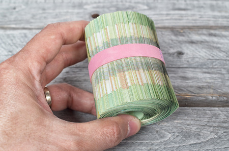 Hand holding a roll full of green bank notes against a wooden background