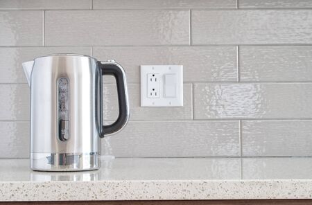 Modern electric stainless steel kettle on a granite counter top against a ceramic background