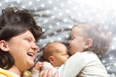mother with two children lying on the bed and enjoying spending time with them