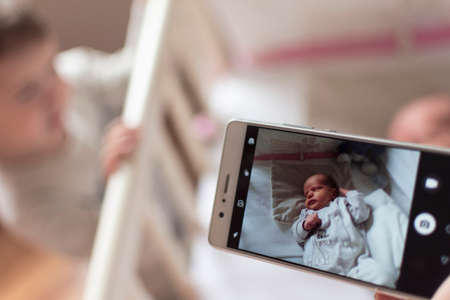 Mother pictures her newborn son while lying in her bedの写真素材