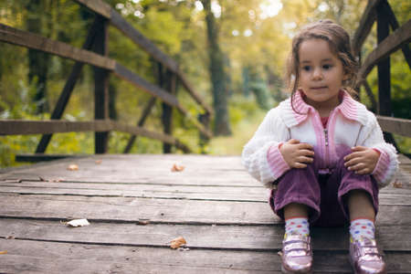 a sweet little girl lying alone sitting on a small wooden bridge in the forestの写真素材
