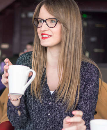 an adult beautiful girl with glasses sits in a bar and drinks tea
