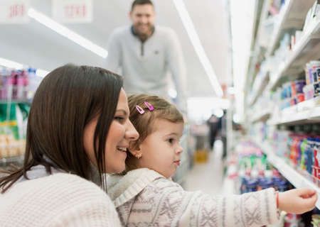 happy family buys at supermarket, mother and daughter close up, father in background pushing shopping cartの写真素材