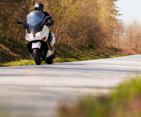 A man enjoys while riding a motorcycle scooter on forest roadsの写真素材