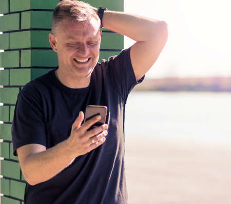 a mature man sends text messages over a mobile phone while standing in the afternoon sun near the lakeの写真素材