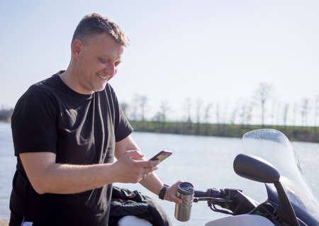 a middle-aged man makes a break on the road near the lake reading and sends text messages on his mobile phone;の写真素材