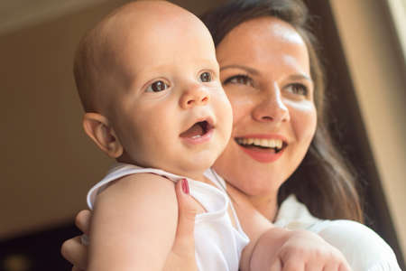 the baby in the mother's arms looks through the window. baby with beautiful facial expressions -...