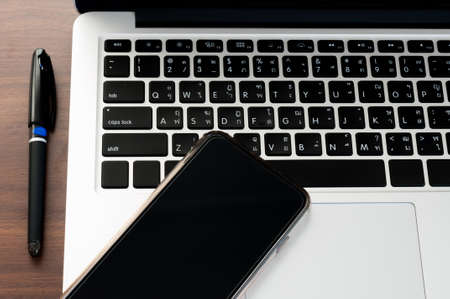 Open laptop with digital smartphone and pen isolated on old wooden desk.の写真素材