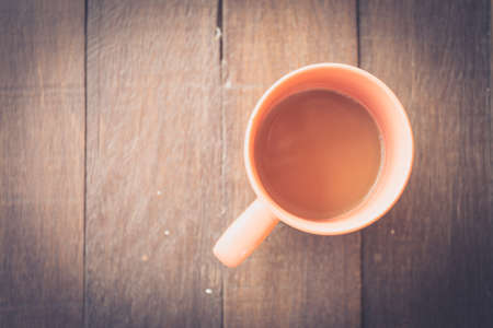 Close up overhead view of a cup of coffee on a rough textured wooden surface with dark vignetting and a highlight around the mug, with copyspaceの写真素材