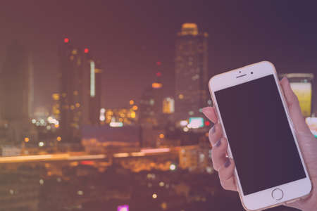 woman hand hold smart phone on abstract bokeh in city scape backgroundの写真素材