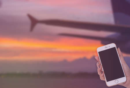 woman hand hold smart phone on aircraft wing, sunrise backgroundの写真素材