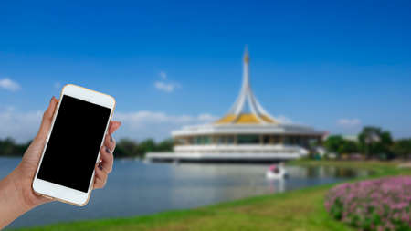 woman hand hold smart phone, blurred public garden background.の写真素材