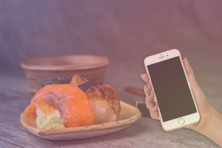 woman hand hold smart phone on blurred japanese sushi setの写真素材