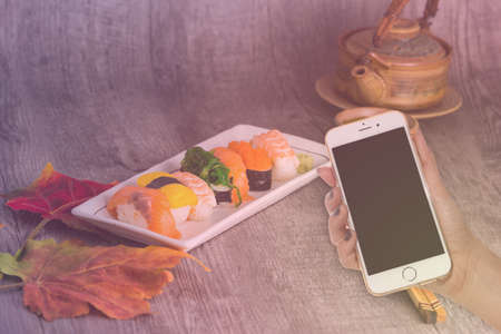 woman hand hold smart phone on blurred japanese sushi setの写真素材