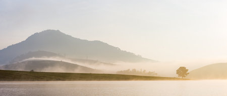 Panoramic view of foggy morning over lake and mountains in backgroundの写真素材
