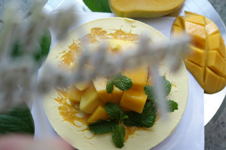 Mango cake with fresh mangoes and mint leaves on white plateの写真素材