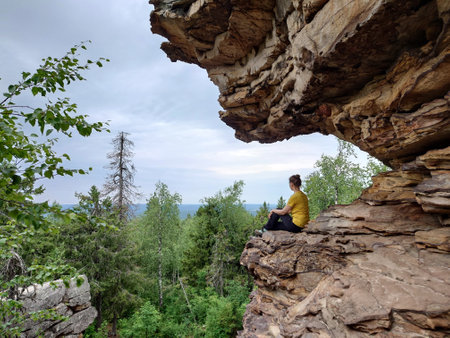 A young woman sits on the edge of a cliff and looks into the distance.の写真素材