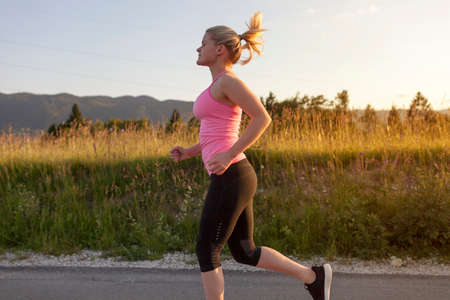 Woman running on the street in suburban area with mountains in the background.の写真素材