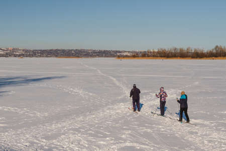 Bright frosty winter day. Frozen River Volga. Group of people skiing.