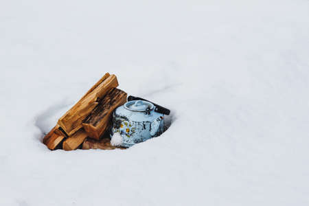 Kettle and firewood in the background of white snowの写真素材