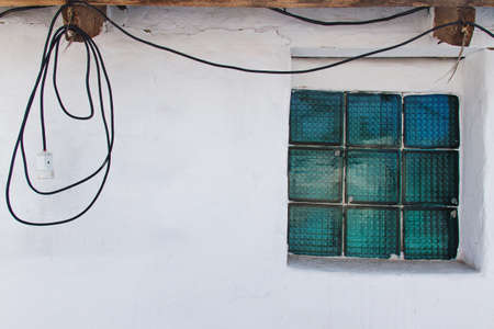 White wall and window of glass blocks and wires hanging at the topの写真素材