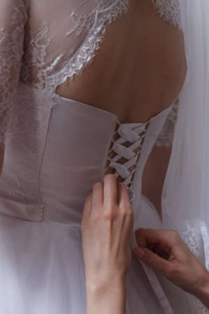 bridesmaid tying bow on bridal wedding dress