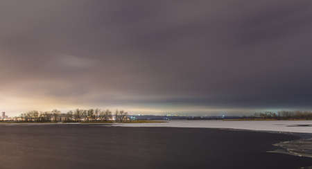 The long exposure of the river is half-bound in the ice and the light from the cityの写真素材