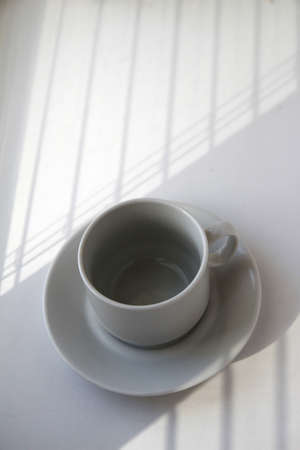 Coffee cup near the window on the background of blinds and shadowsの写真素材