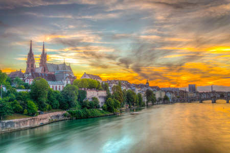Sunset view of riverside of Rhine in Basel dominated by majestic building of Munster church,...