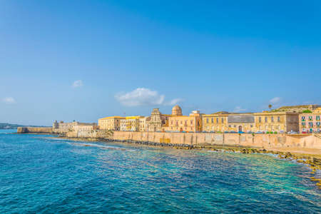 View of the seaside promenade surrounding the old town of Syracuse in Sicily dominated by chiesa dello spirito santo and castello maniace, Italyの写真素材
