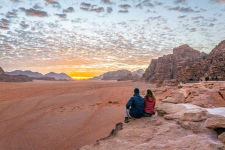 A young couple is watching at sunrise over wadi rum desert in Jordanの写真素材