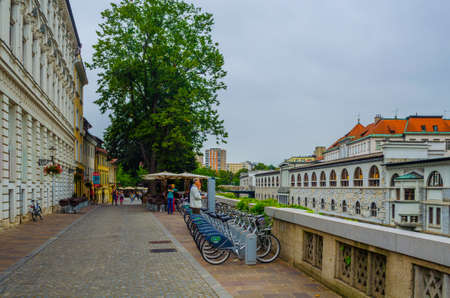 LJUBLJANA, SLOVENIA, July 29, 2015: people walk along Petkovskovo Waterfront with shops and restaurants in front of Market Place and Butcher Bridge over Ljubljanica river.のeditorial素材
