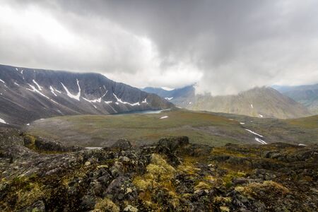 The Subpolar Urals. The Lake and field between mountains under clouds