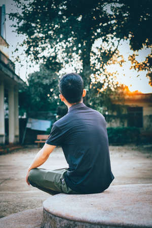 Young man sitting on a stone bench in the evening, back viewの写真素材