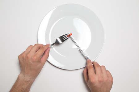 Man eating a red pill from a white plate with knife and fork, isolated on white background. Concept of  eating pills like food. Copy space.の写真素材