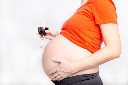 Pregnant women with glass of wine, concept of unhealthy lifestyles during pregnancy and motherhood. Isolated in white background.の写真素材