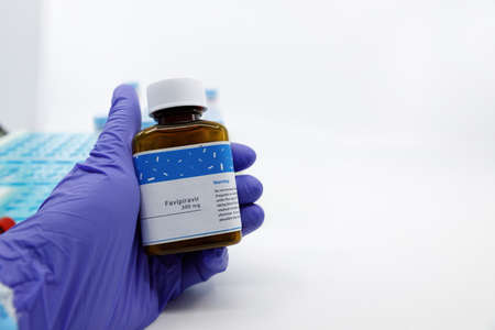Dubai-UAE-Circa 2020:Doctor showing bottle of medicine for covid-19 treatment.Concept of Favipiravir medicine with blood tests tubes on the background.Cure for coronavirus,COVID-19 treatment.のeditorial素材