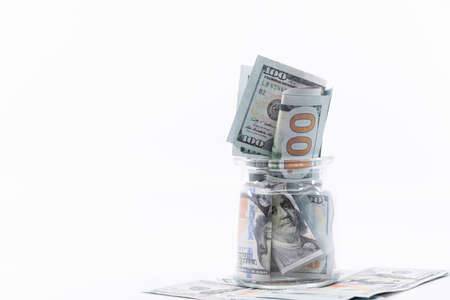 Jar full and over flowing with hundred dollar bill banknotes sitting on big pile of money. White negative space, copy space. Concept saving money for finance accounting, retirement, schooling.の写真素材