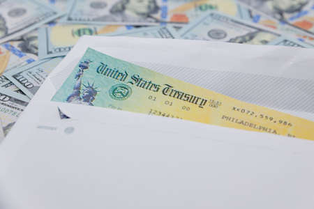 Stack of 100 dollar bills with coronavirus stimulus payment check to show the virus payment to Americans. Concept IRS tax refund or coronavirus stimulus payments. Global pandemic Covid 19 lock downの写真素材