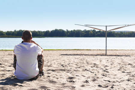 A guy with a thoughtful look sits on the beach looking into the distanceの写真素材