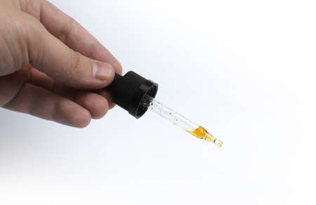Eyedropper with dark liquid in hand on a white background isolatedの写真素材