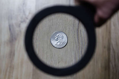 A magnifying glass is aimed at a quarter of a dollar on a wooden parquetの写真素材