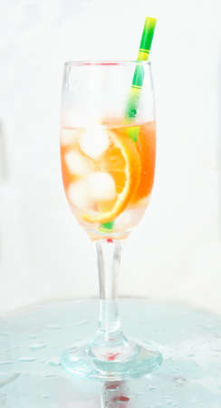 champagne glass with cocktail oranges with ice green straw on wet glass light background
