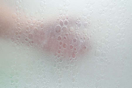 hand through a shower screen with drops on a light backgroundの写真素材