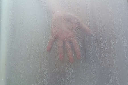 hand through a shower screen with drops on a light backgroundの写真素材
