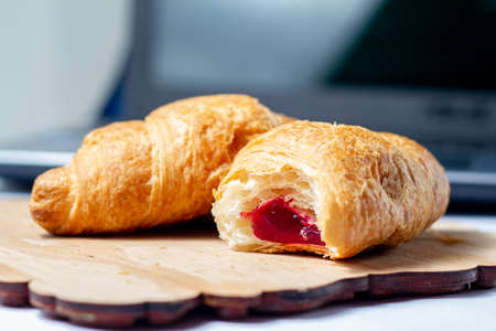 croissants bitten with strawberry jam with dry wheat on a wooden board on a laptop backgroundの写真素材