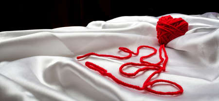 white silk fabric with bends and a red knitted heart with nicknames for Valentine's Day, copy space